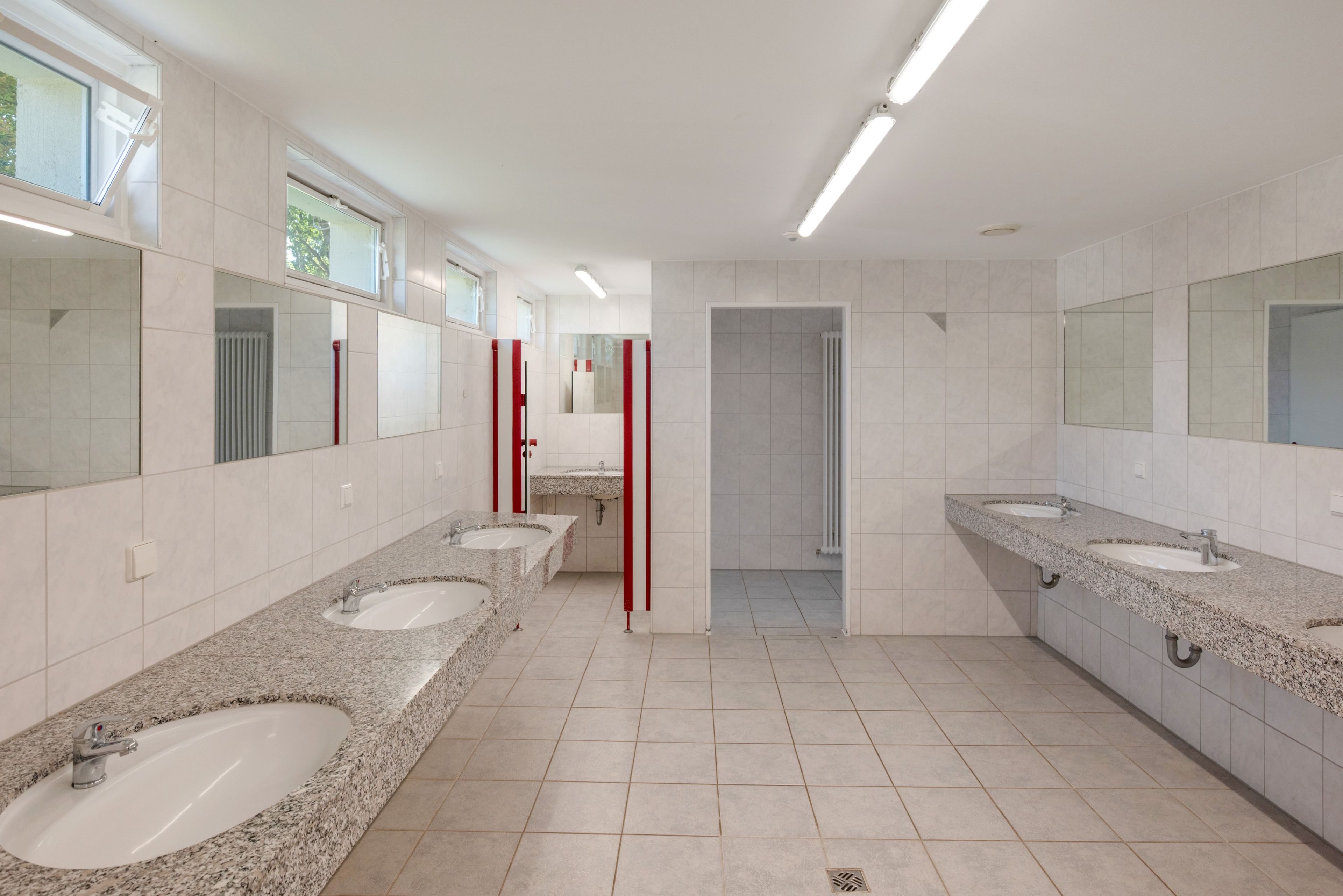Een openbaar toilet met meerdere wasbakken, spiegels en een douchegedeelte.