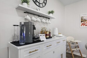 En tekøkken med kaffemaskine, vanddispenser og opbevaringsskabe.