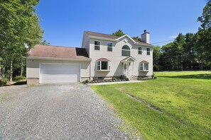A two-story house with a garage, a front porch, and a well-maintained lawn. - Pocono Oasis | Hot Tub • Game Room • Fenced Yard (Long Pond)