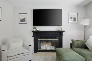 Una sala de estar con chimenea, un sofá, un sillón y un televisor montado en la pared.