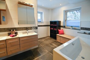 Une salle de bain moderne avec une baignoire, un meuble-lavabo avec des tiroirs, une étagère avec des serviettes et un grand miroir.