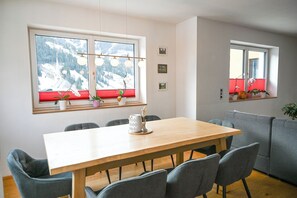 A dining area with a wooden table, grey chairs, and a window with red blinds.