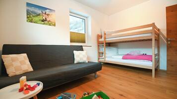 Ein Zimmer mit Etagenbett, einer Schlafcouch, einem kleinen Tisch mit Spielzeug und einem Fenster mit Jalousien.