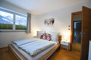 A bedroom with a bed, a nightstand, a lamp, a window with curtains, and a door.