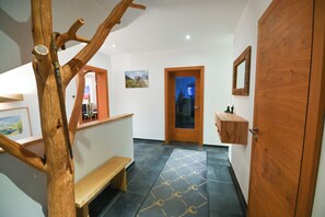 A hallway with a wooden bench, a door, a mirror, and a tiled floor.