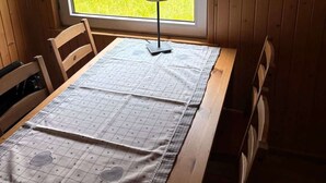 A wooden table with a checkered tablecloth, a lamp, and a window with a view of a green field.