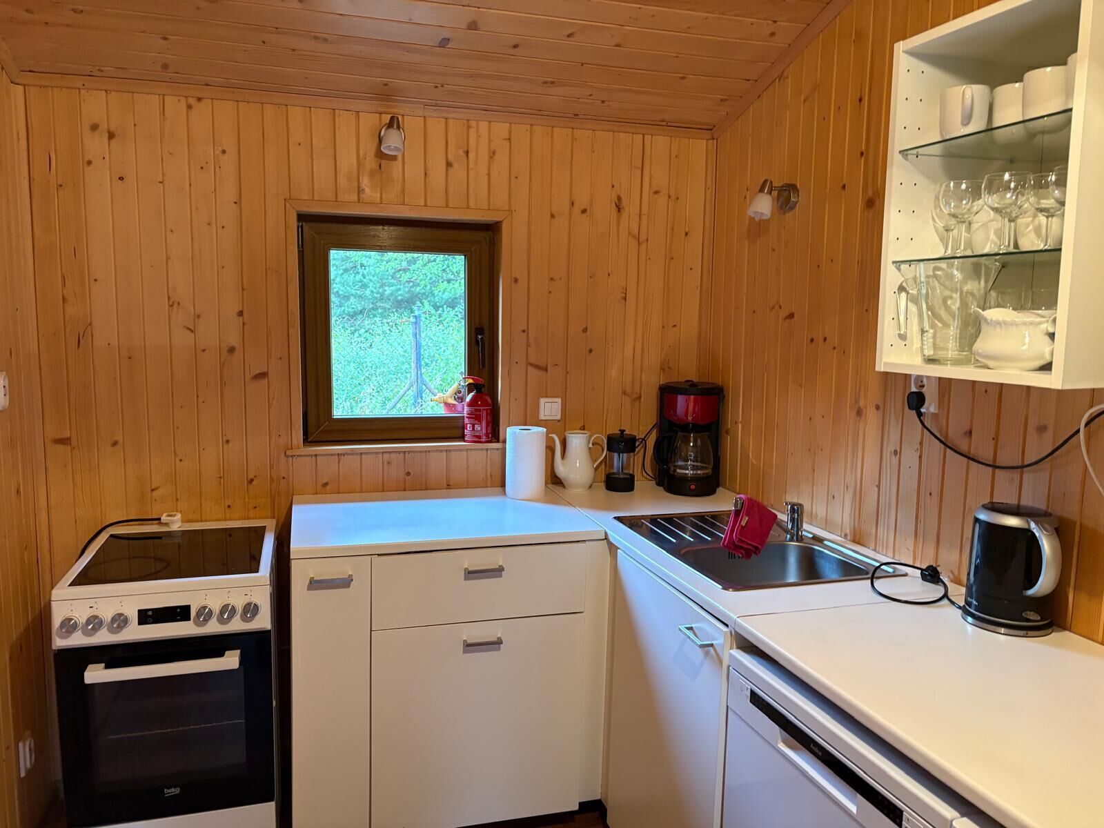 Uma cozinha compacta com fogão, forno, pia e uma janela com vista para o verde.