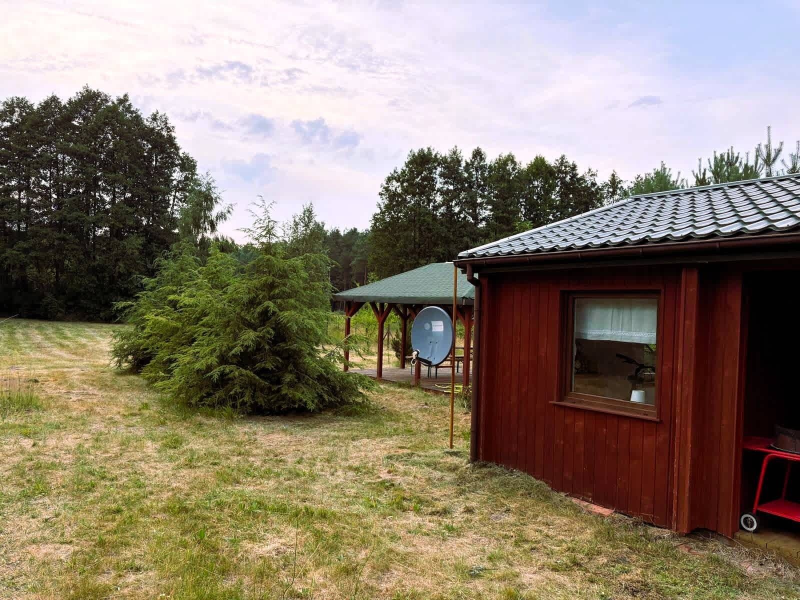 A wooden cabin with a tiled roof, surrounded by a grassy area and trees.