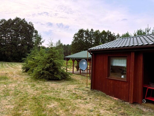 A wooden cabin with a tiled roof, surrounded by a grassy area and trees.