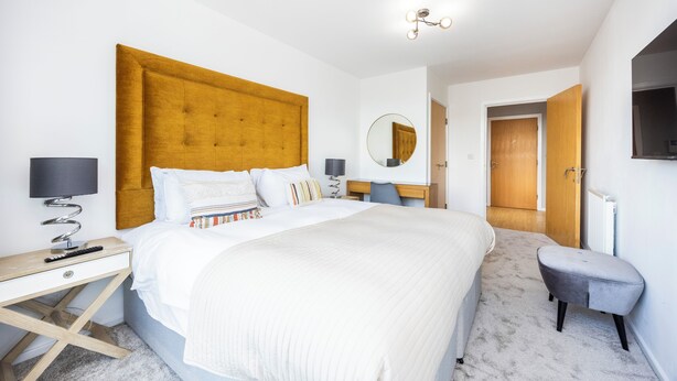 A modern hotel room with a large bed, a desk, a chair, and a TV mounted on the wall. - Vintage Pad  (London)