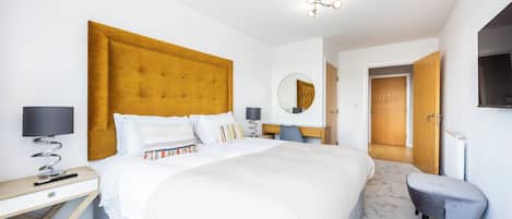 Una habitación de hotel moderna con una cama grande, un escritorio, una silla y un televisor fijado a la pared.