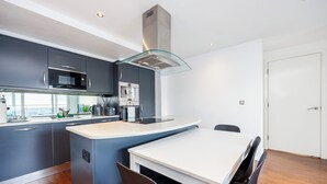 A modern kitchen with dark cabinetry, a white countertop, and a glass hood. - Vintage Pad  (London)