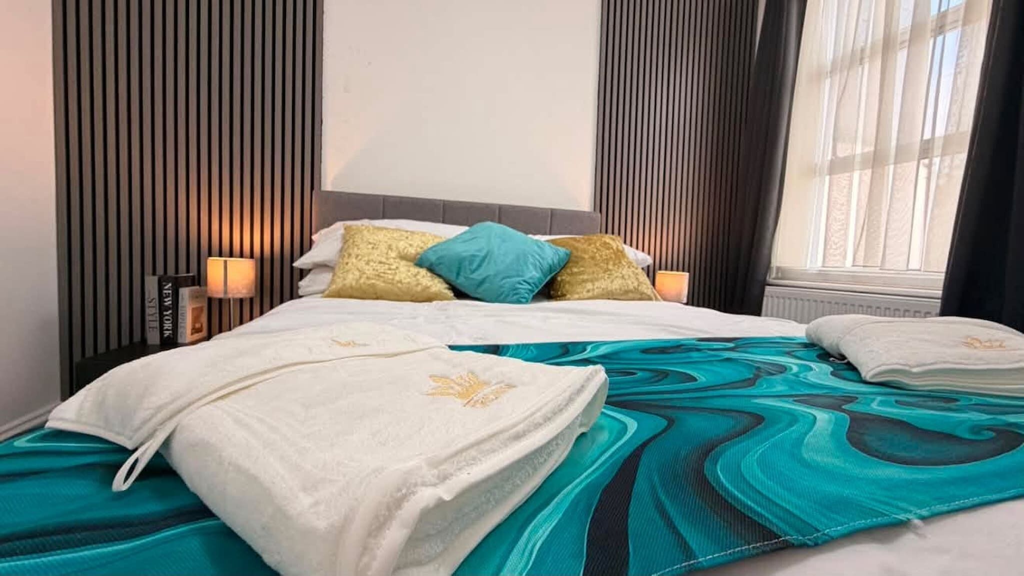 A hotel room with a bed, pillows, a blanket, and a nightstand with a lamp.