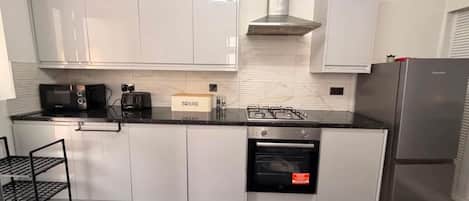 A modern kitchen with white cabinets, a black countertop, a built-in oven, and a stainless steel range hood.