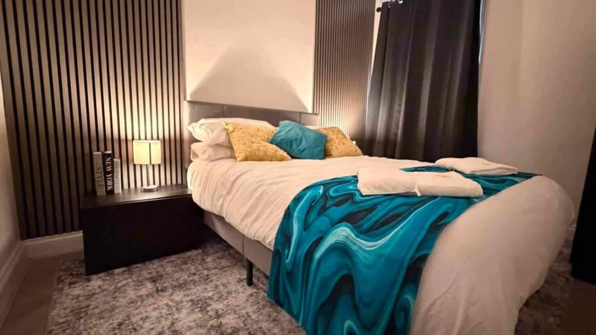 Et hotelværelse med en seng, et natbord, en lampe og et vindue med gardiner.