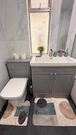 A bathroom with a toilet, sink, and cabinet. - Stylish 3BR House in Newham East London (London)
