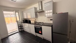 A modern kitchen with white cabinets, a gas stove, a built-in oven, and a stainless steel refrigerator. - Stylish 3BR House in Newham East London (London)