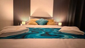 A hotel room with a bed, pillows, a blue patterned bedspread, and two bedside lamps. - Stylish 3BR House in Newham East London (London)