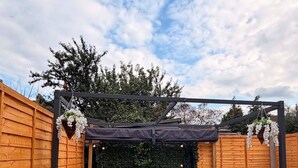 A hot tub in a wooden deck area with a pergola overhead. - Stylish 3BR House in Newham East London (London)