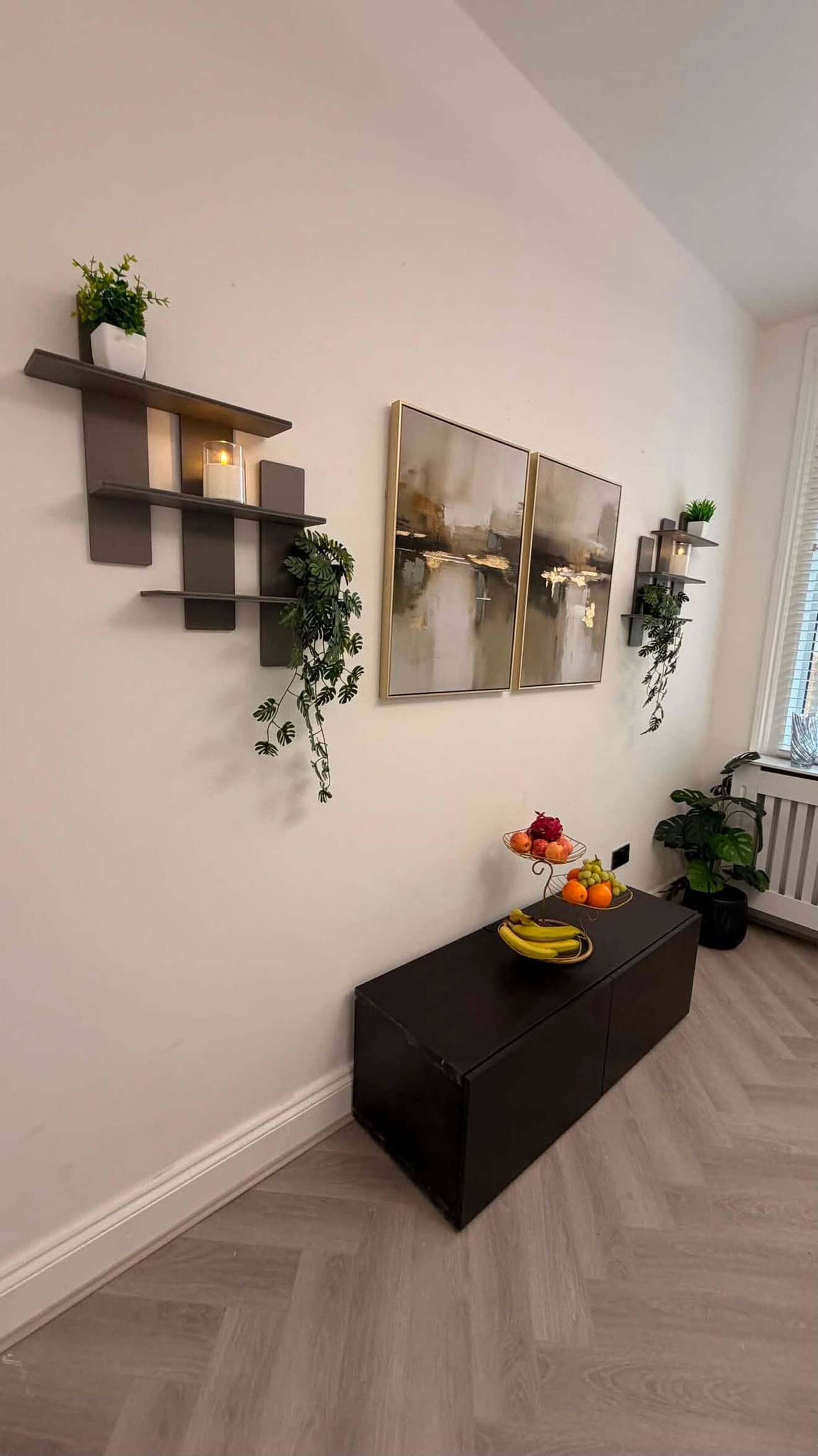 Una sala de estar moderna con una consola negra, detalles decorativos en la pared y plantas en macetas.