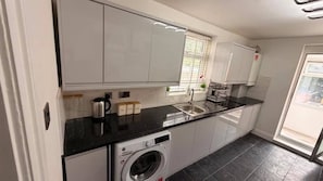 Eine moderne Küche mit weißen Schränken, einer schwarzen Arbeitsplatte, einer integrierten Waschmaschine und einem Fenster mit Jalousien.