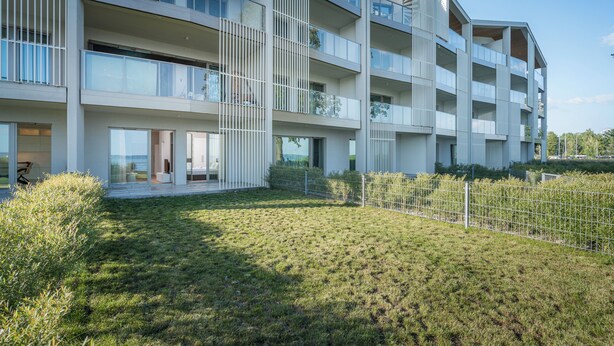 Un moderno edificio residencial de varios pisos con balcones, ventanas amplias y un césped bien cuidado.