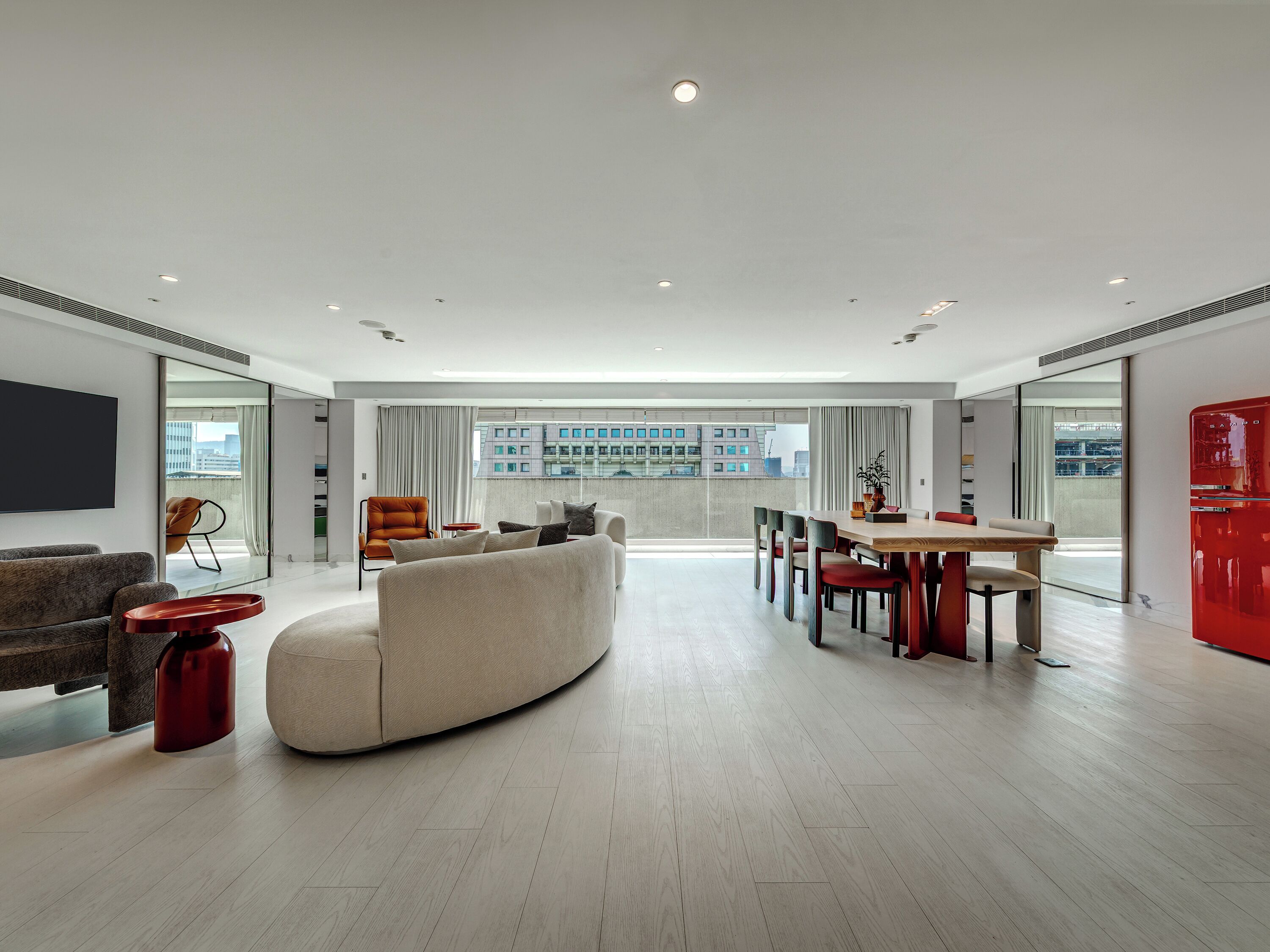 A modern living room with a large sofa, a dining table, and a red refrigerator.
