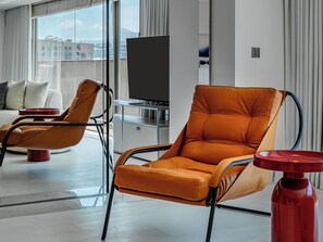 A modern hotel room with a large window, a sofa, two orange armchairs, a flat-screen TV, and a red side table. - OOD Hotel Taipei Dunhua North (Taipei)