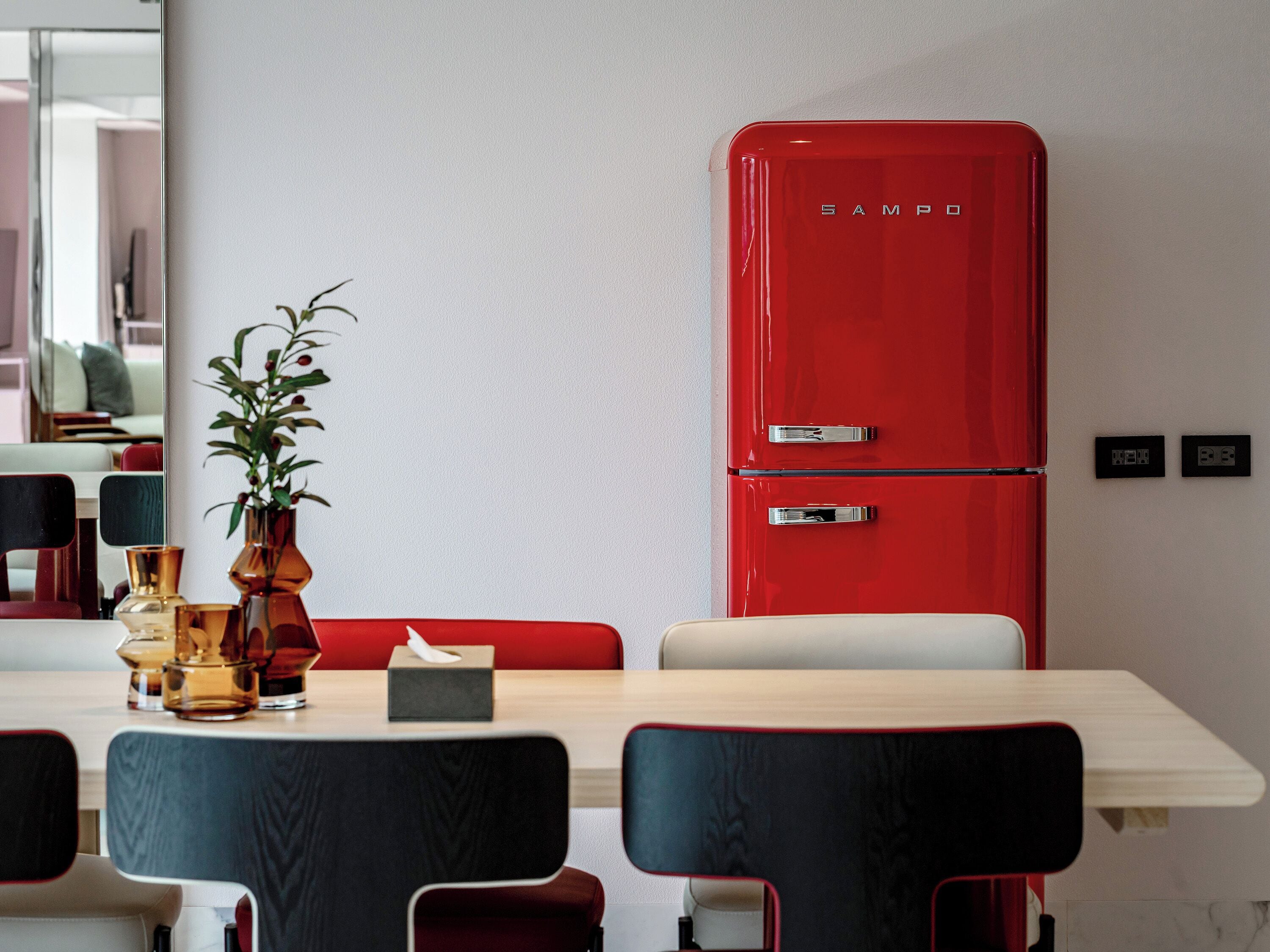 Un comedor con un refrigerador rojo, un florero y una caja de pañuelos sobre la mesa.