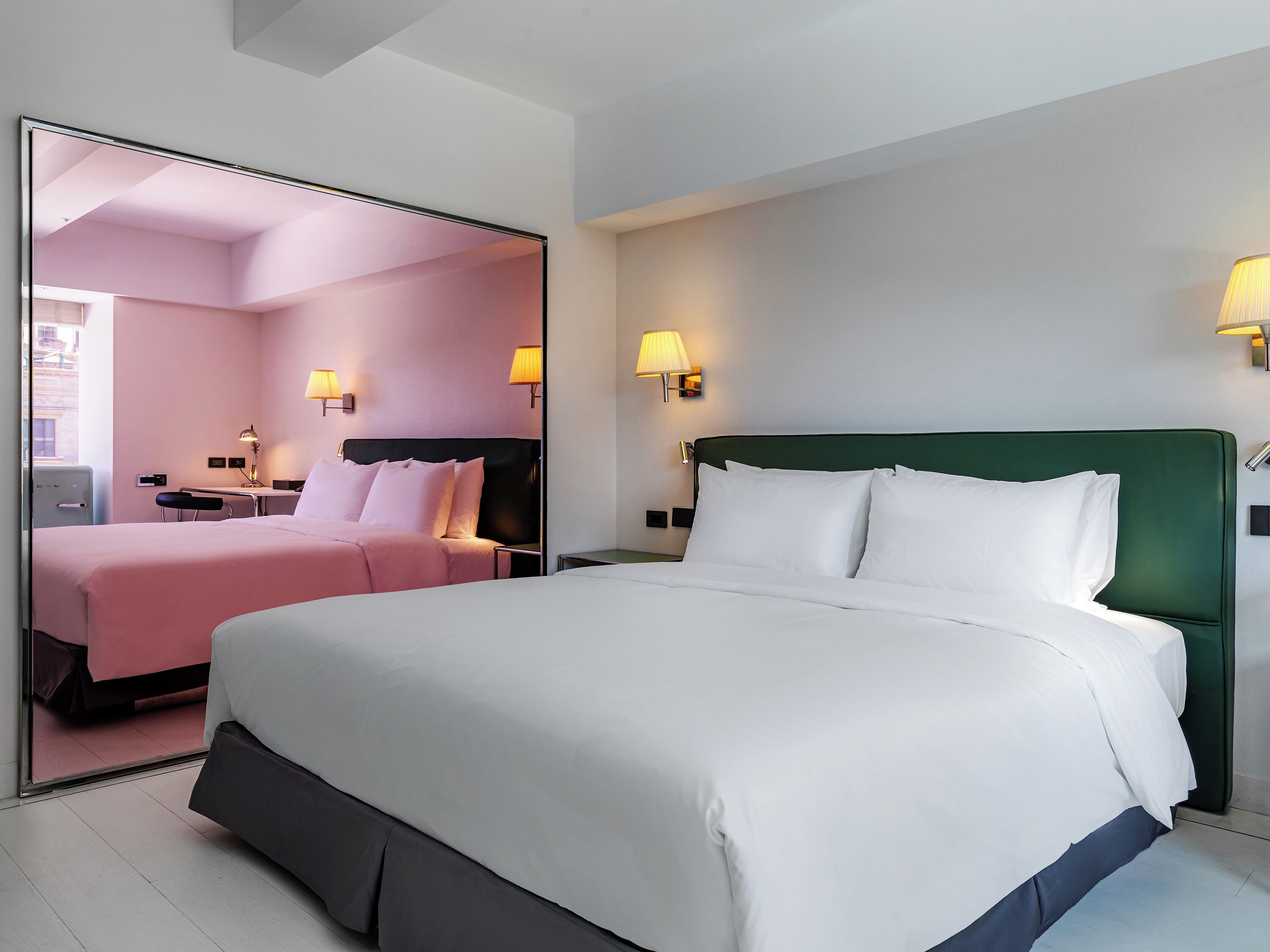Une chambre d’hôtel avec un grand lit, des tables de chevet, des lampes et un miroir.