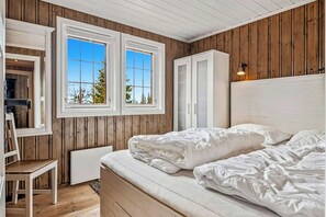 A bedroom with a bed, a chair, a wardrobe, and two windows.