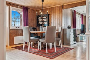 A dining area with a wooden table, four chairs, a chandelier, and a red rug.