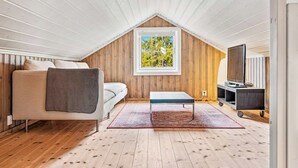 Acogedor dormitorio en ático con techo inclinado, un sofá, una pequeña mesa, un televisor y una ventana con vistas a árboles.
