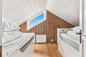 Ein kleines Schlafzimmer im Dachgeschoss mit zwei Betten, einem Fenster und Holzwänden.