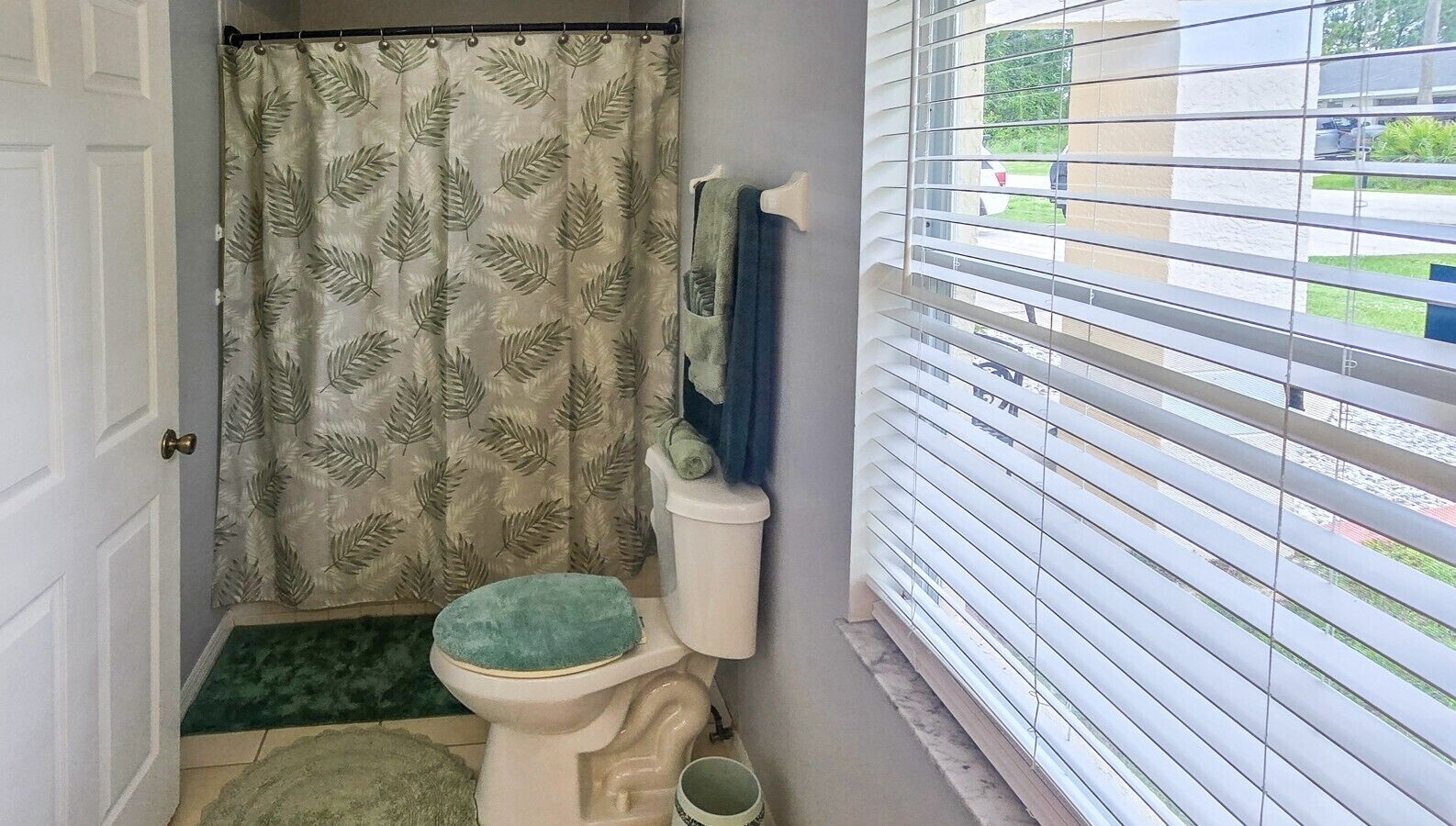 A bathroom with a toilet, a shower curtain, and a window with blinds.
