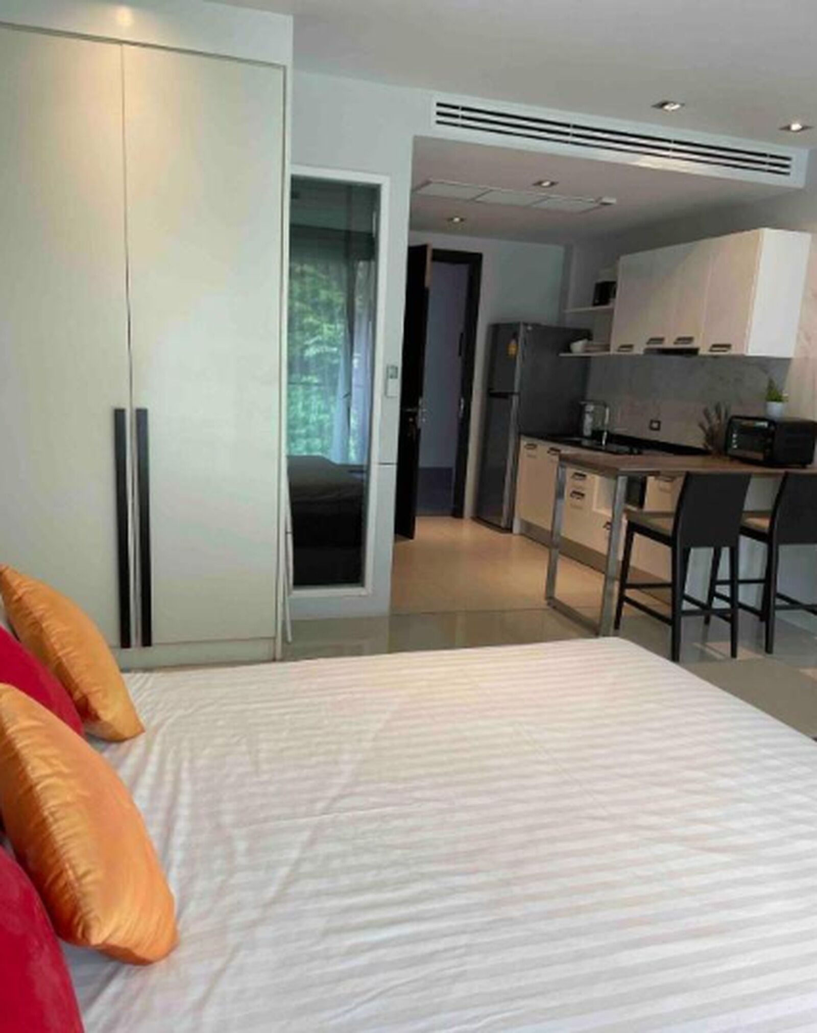 A modern bedroom with a bed, a desk, and a kitchenette.