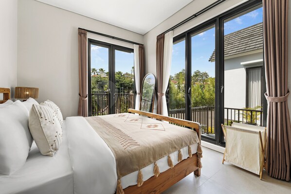 A bedroom with a bed, a small table, and a view of the outdoors.