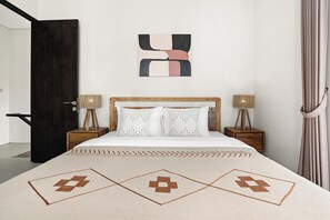 A bedroom with a bed, two bedside tables, a wooden headboard, a wall-mounted abstract art piece, and a curtain.