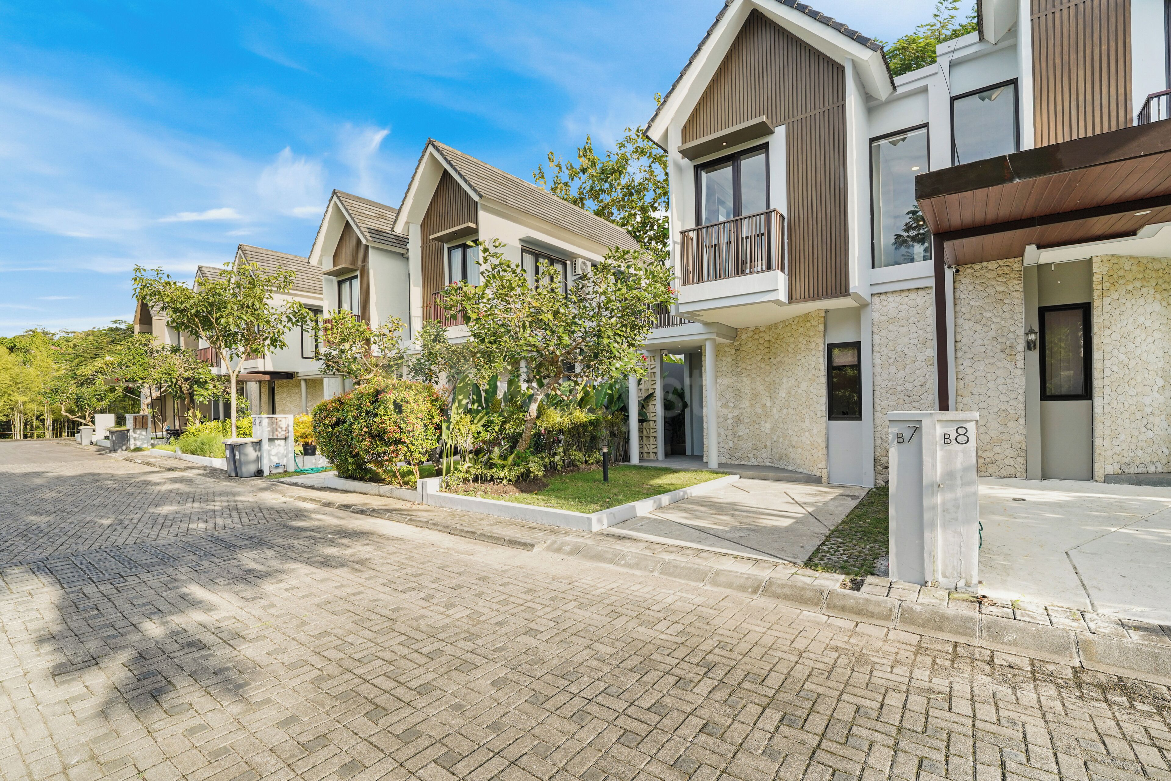 A residential street with modern houses, paved sidewalks, and greenery.