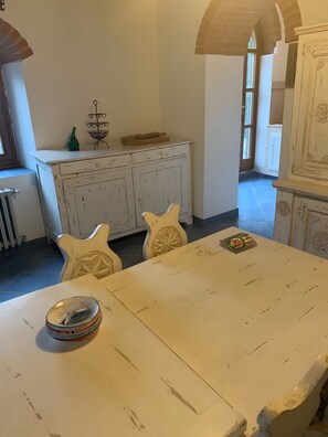 A dining area with a white table, two chairs, and a cabinet with a metal rack on top. - Country House 'Le Mulina' with Wi-Fi (Barberino di Mugello)