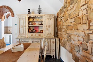 Une pièce rustique avec un mur en pierre, une table en bois et un meuble blanc agrémenté d’objets décoratifs.