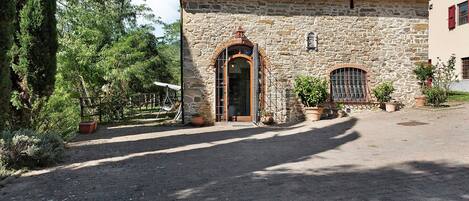 Un edificio de piedra con tejado de baldosas, un arco central y una ventana pequeña con barrotes.