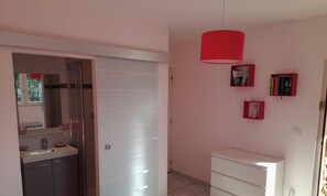 Ein Zimmer mit einem weißen Kleiderschrank, einer roten Hängeleuchte und zwei roten Bücherregalen mit Büchern.