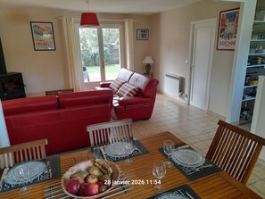 Ein Wohnzimmer mit einem roten Sofa, einem Esstisch mit Platzsets und Weingläsern sowie einer Obstschale.