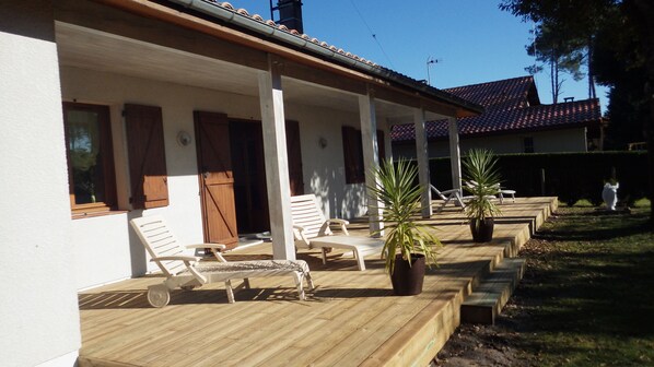 A covered outdoor seating area with wooden loungers and potted plants. - Vrbo Property (Messanges)