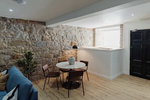 A room with a stone wall, a round table with chairs, a potted plant, and a black door. - Joivy Vaults Studios and Apartments (Edinburgh)