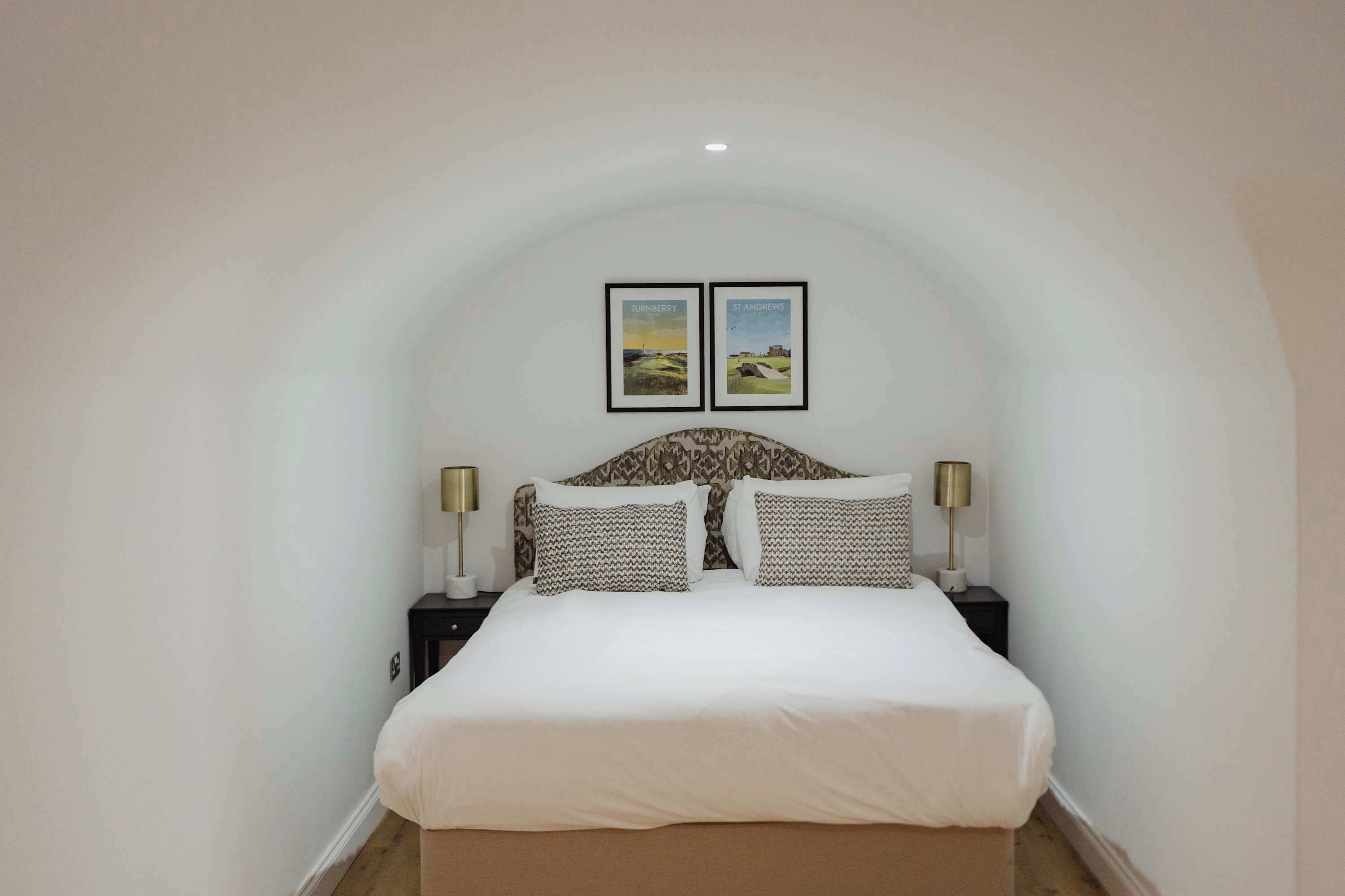 A bedroom with a white bed, patterned pillows, two framed pictures on the wall, and bedside lamps.