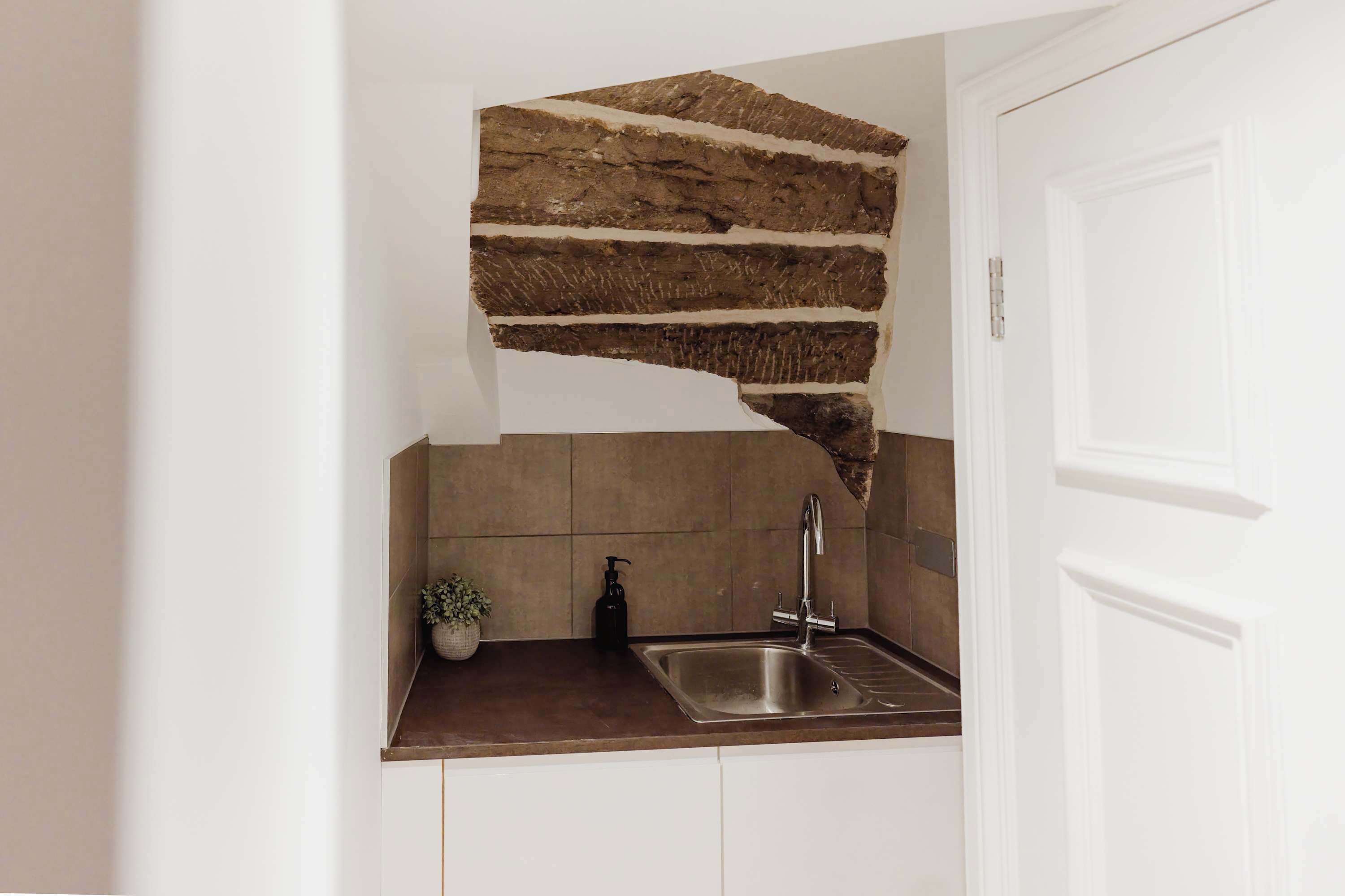 A kitchen with a unique stone backsplash, a sink, and a potted plant.