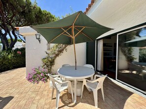 An outdoor patio with a round table, two chairs, a green umbrella, and a white wall with a window. - Vilamoura Vintage Villa by Homing (Loulé)