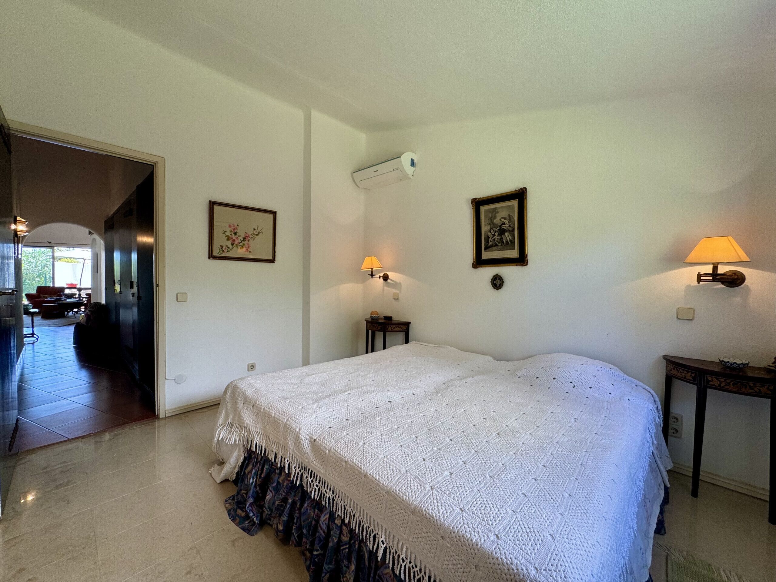 Une chambre à coucher avec un grand lit, une table de chevet, une lampe et un climatiseur fixé au mur.